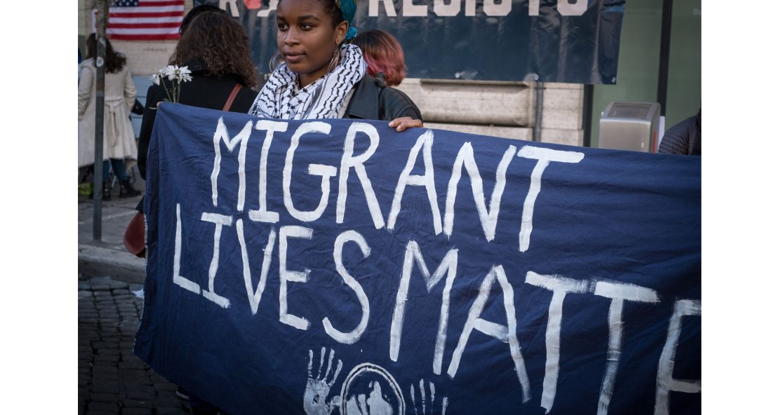 A woman in Rome holds a sign reading "Migrant Lives Matter."