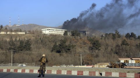 An Afghan security official stands guard as black smoke rises from the Intercontinental Hotel Sunday.