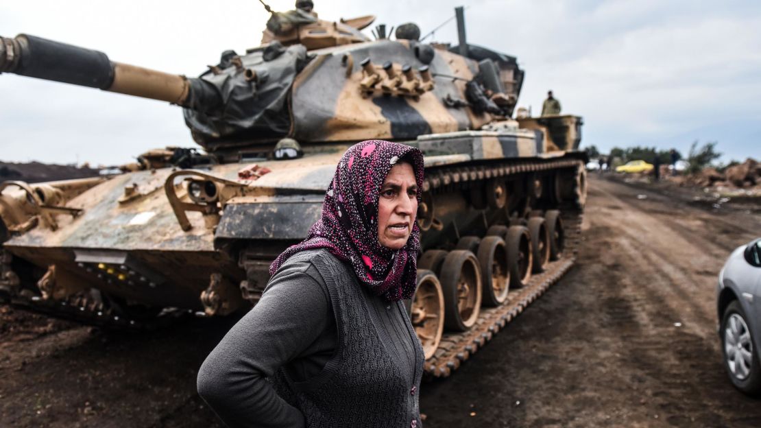 A Turkish villager stands next to Turkish army tanks as soldiers gather close to the Syrian border.