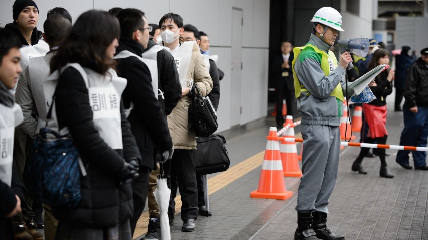 Participants stand outside a subway entrance as a worker with the Tokyo Metropolitan Government gives directions before the start of Monday's missile-attack drill in Tokyo.