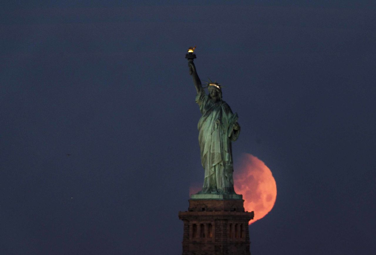 The supermoon sets behind the Statue of Liberty in New York.