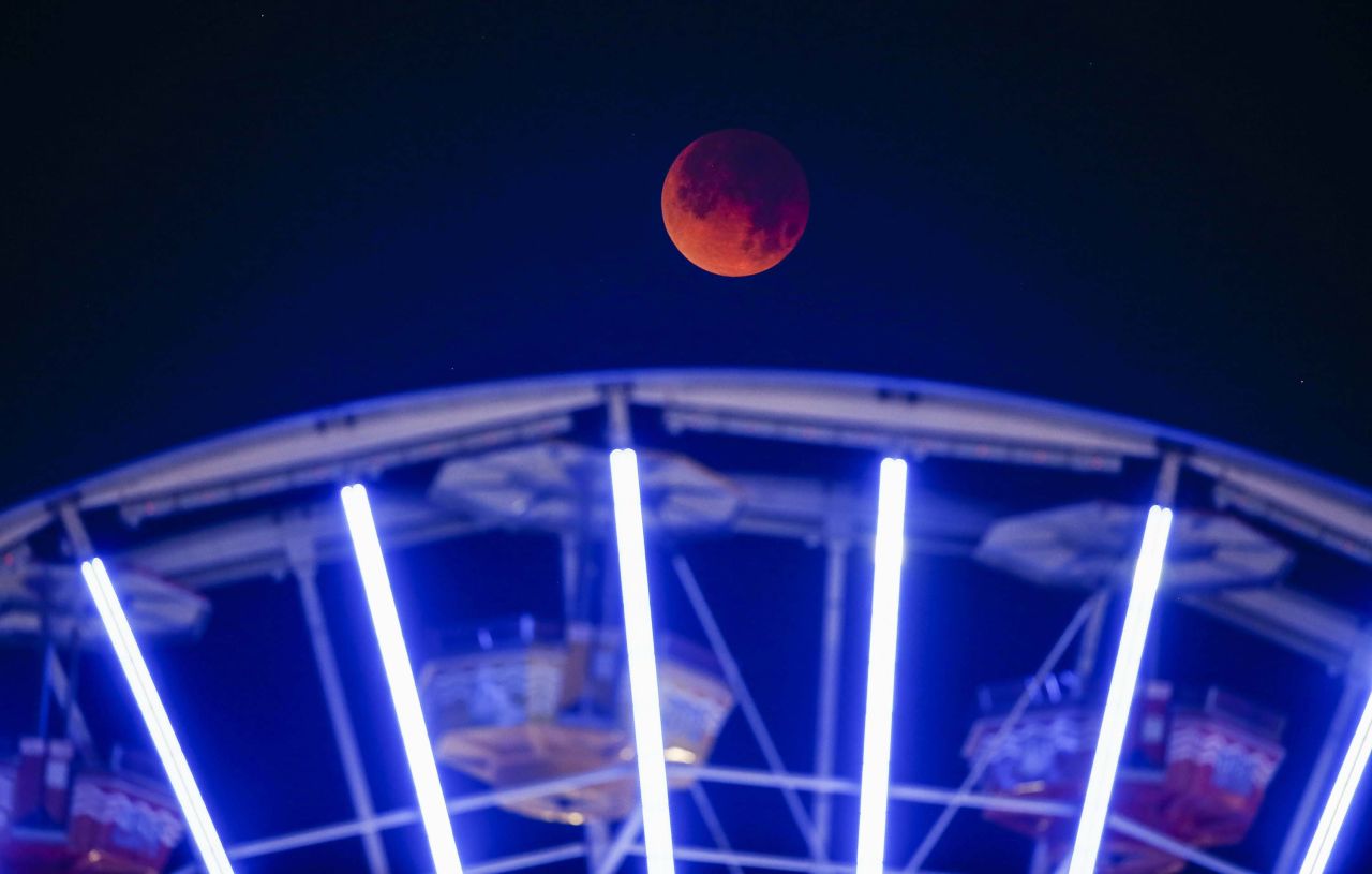 The moon is seen behind a Ferris wheel at Santa Monica Beach in Santa Monica, California.