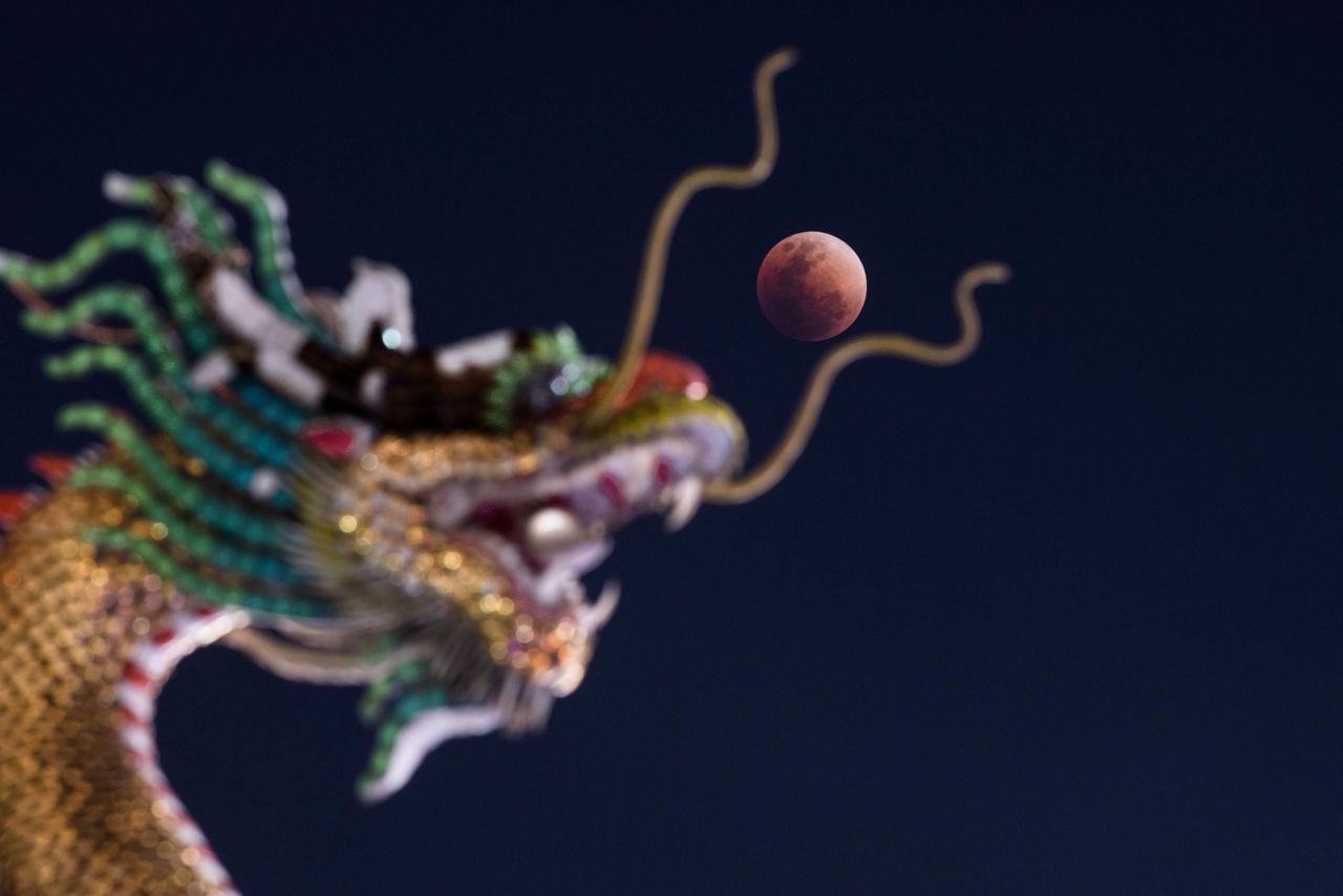 The moon rises over the head of a Chinese dragon statue at a Buddhist temple in Bangkok, Thailand.