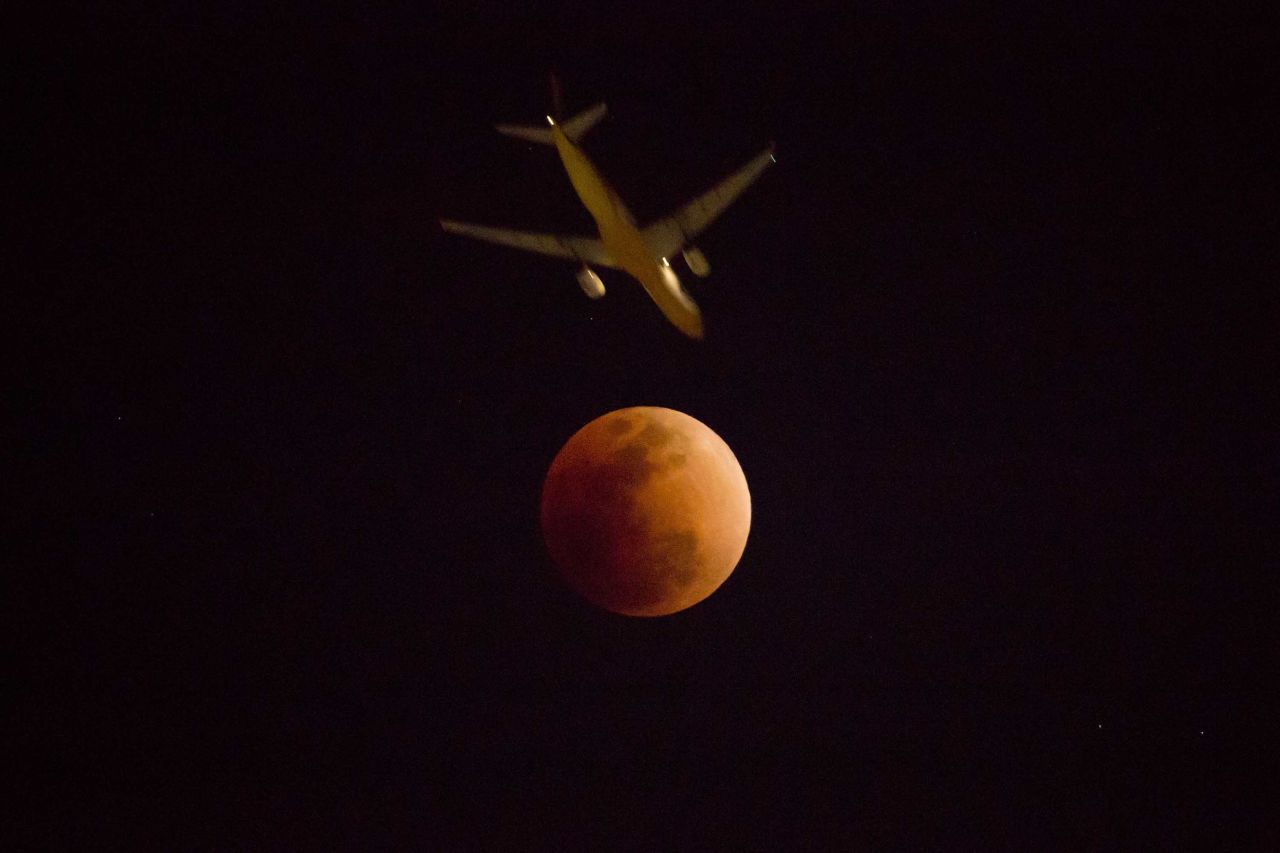 A plane flies into view with the moon in Hong Kong.