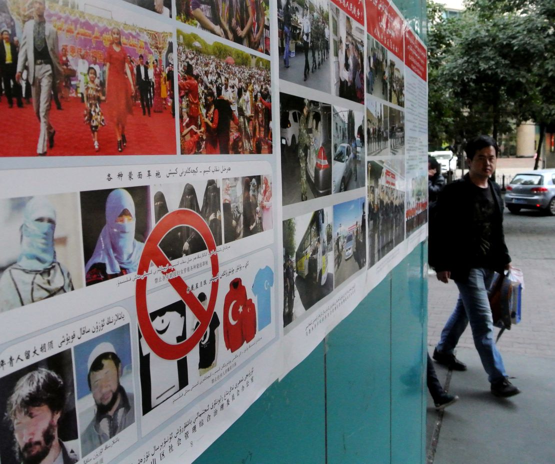 Pedestrians walk past anti-terror propaganda posters pasted along the streets of Urumqi,  September 2014.