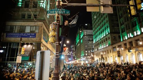 A man climbs a traffic pole as Philadelphia Eagles fans celebrate victory. 