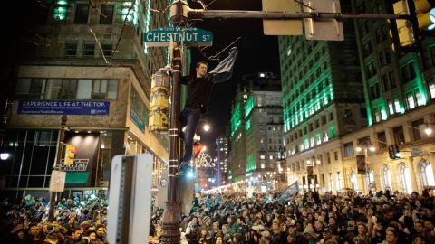 A man climbs a traffic pole as Philadelphia Eagles fans celebrate victory.