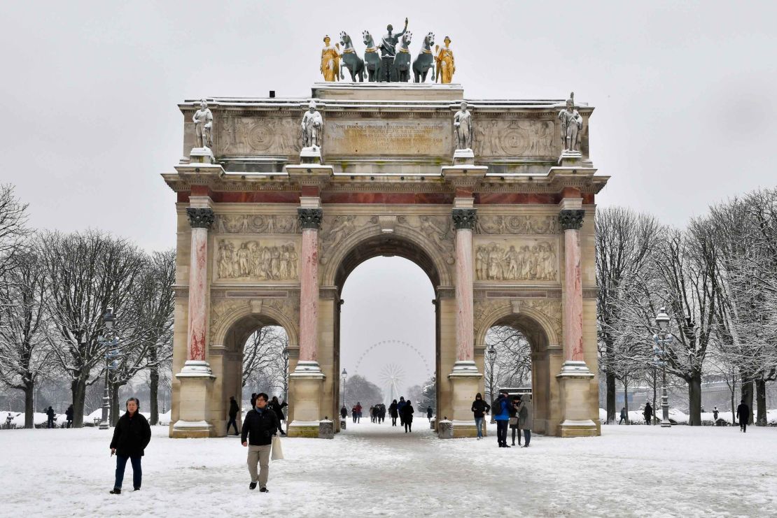 People pass by the Arc de Triomphe du Carrousel as they walk through the snow covered Tuileries garden.