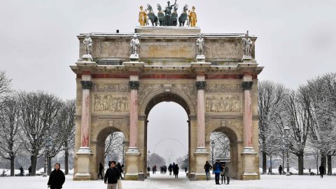 People pass by the Arc de Triomphe du Carrousel as they walk through the snow covered Tuileries garden.