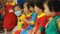 A masked girl sits with classmates at a kindergarten in a residential estate in Hong Kong on June 11, 2009. Hong Kong authorities on June 11 ordered all primary schools in the city to be closed for two weeks after the first cluster of local swine flu cases was found. The move came after 12 pupils at a city secondary school were found to have contracted the A(H1N1) virus, chief executive Donald Tsang told reporters. AFP PHOTO/MIKE CLARKE (Photo credit should read MIKE CLARKE/AFP/Getty Images)
