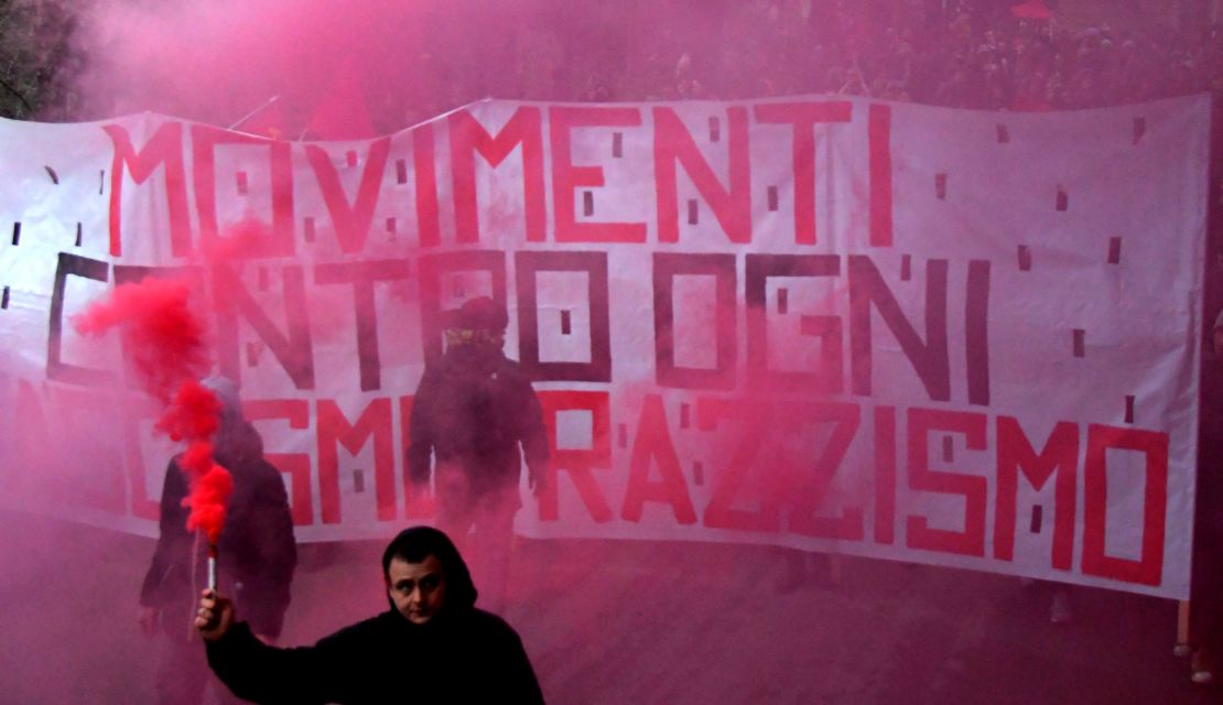 A man holds a flare in front of an anti-fascism banner during a protest Saturday in Macerata.