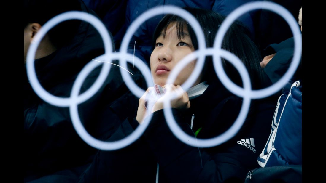 The Olympic rings are reflected by glass as a spectator watches a curling match.