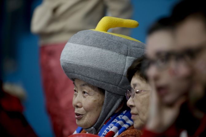 A curling spectator wears a hat shaped like a curling stone.