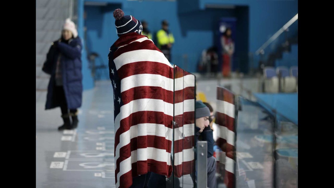 A spectator draped with an American flag watches a men's curling match.