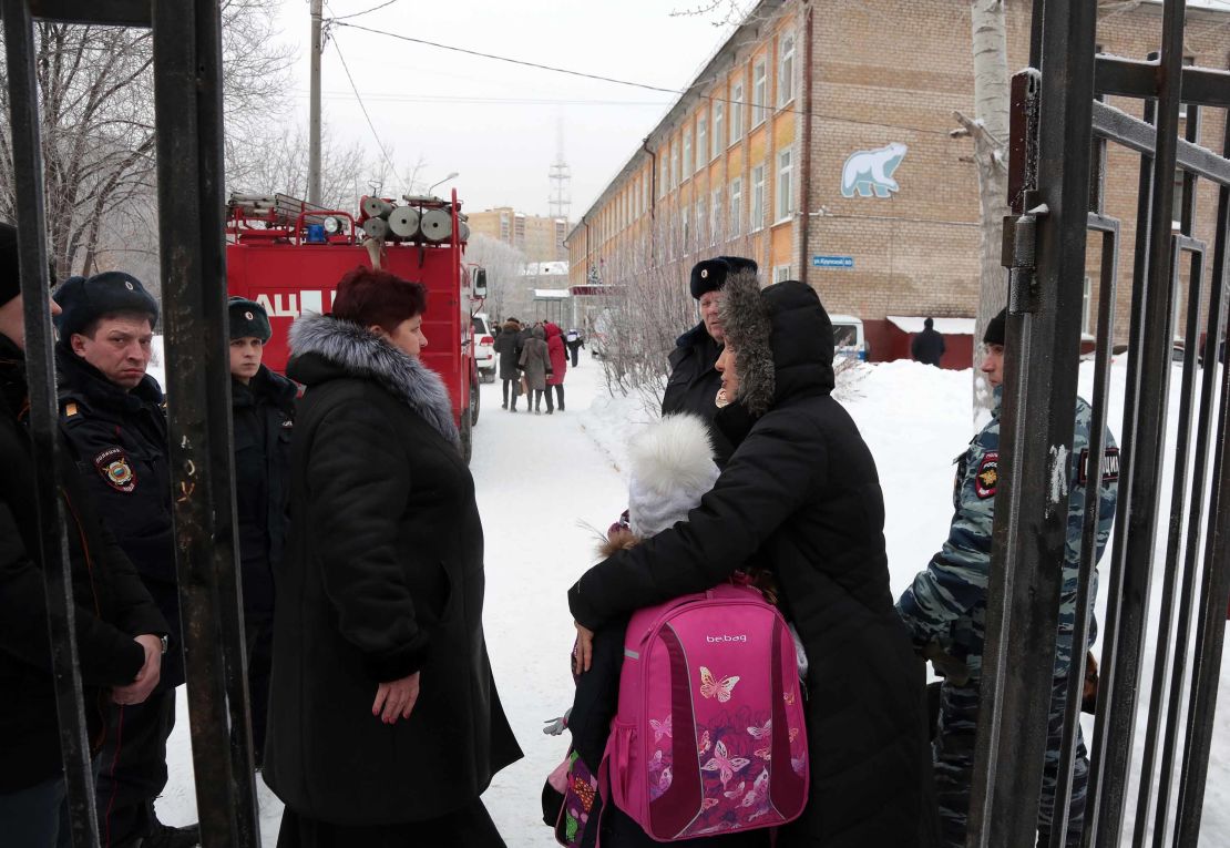 Parents with children and police stand outside the school in Perm where a knife attack left a teacher and several students injured.