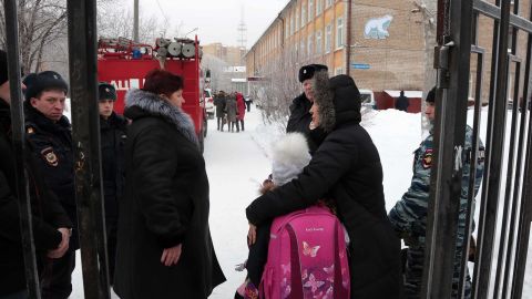 Parents with children and police stand outside the school in Perm where a knife attack left a teacher and several students injured.