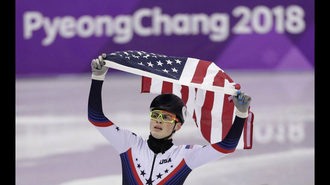Short-track speedskater John-Henry Krueger celebrates with the American flag after winning silver in the 1,000 meters. Canada's Samuel Girard won the gold.