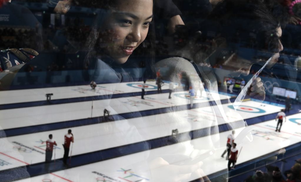 A woman's reflection can be seen as she watches a men's curling match.