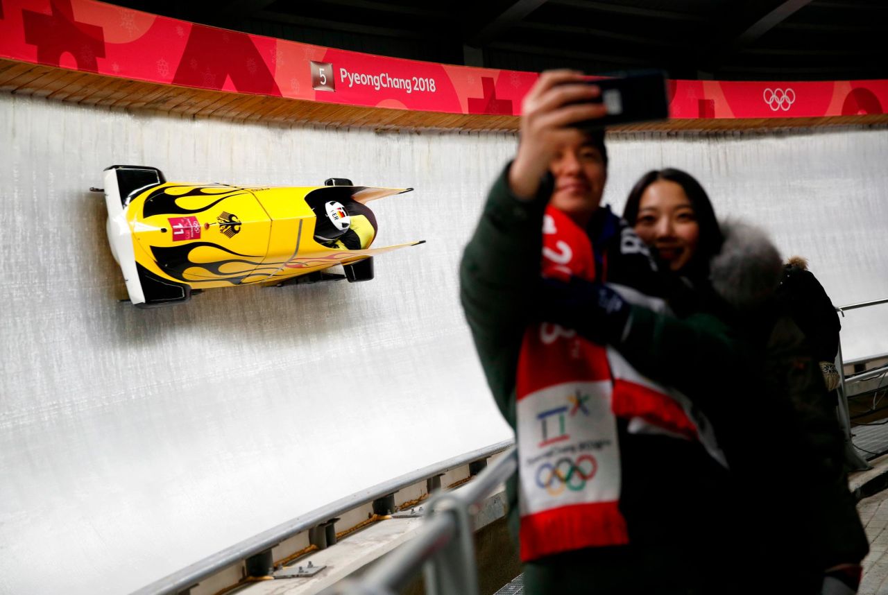 A couple takes a selfie as the German bobsled duo, Nico Walther and Christian Poser, pass by