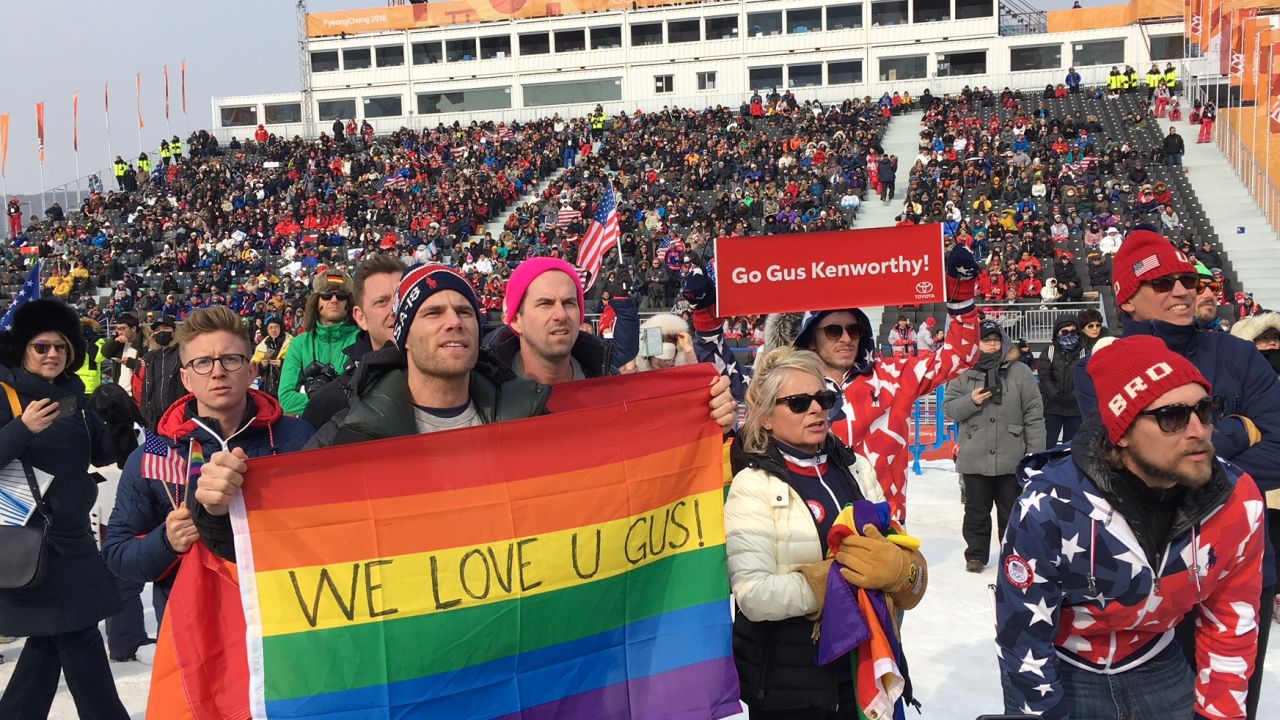 Gus Kenworthy's boyfriend Matthew Wilkas holds the rainbow flag as he watches the action.