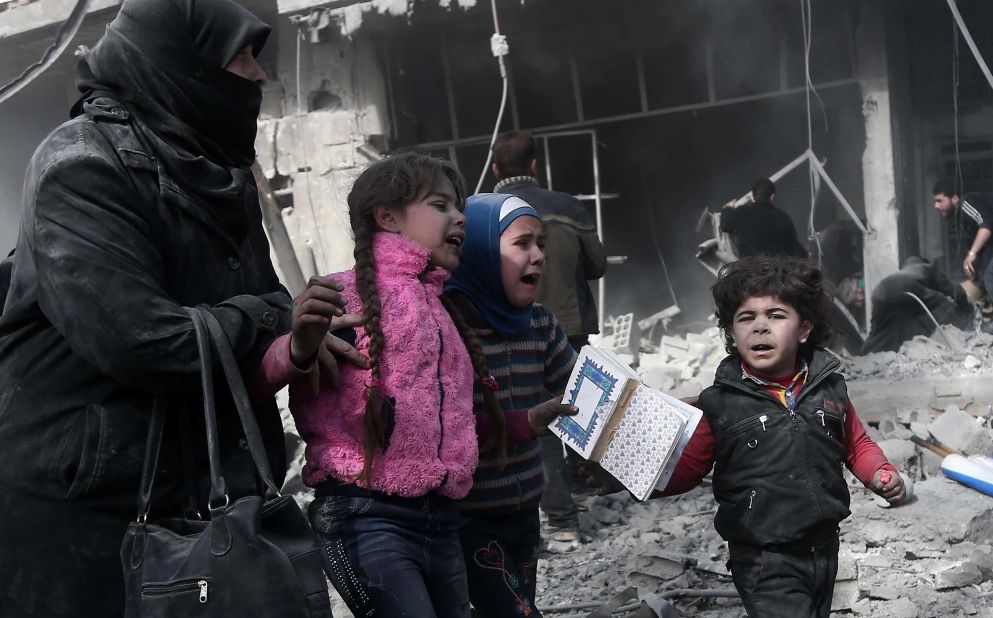 A woman and children run for cover after bombing in Hamouria on Monday, February 19.