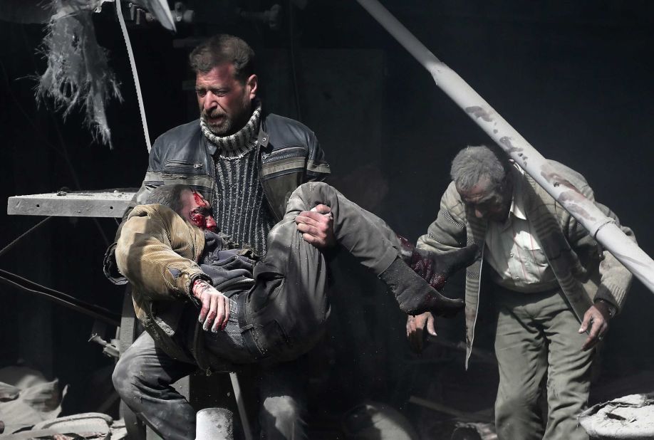 A man carries an injured victim amid the rubble of buildings.