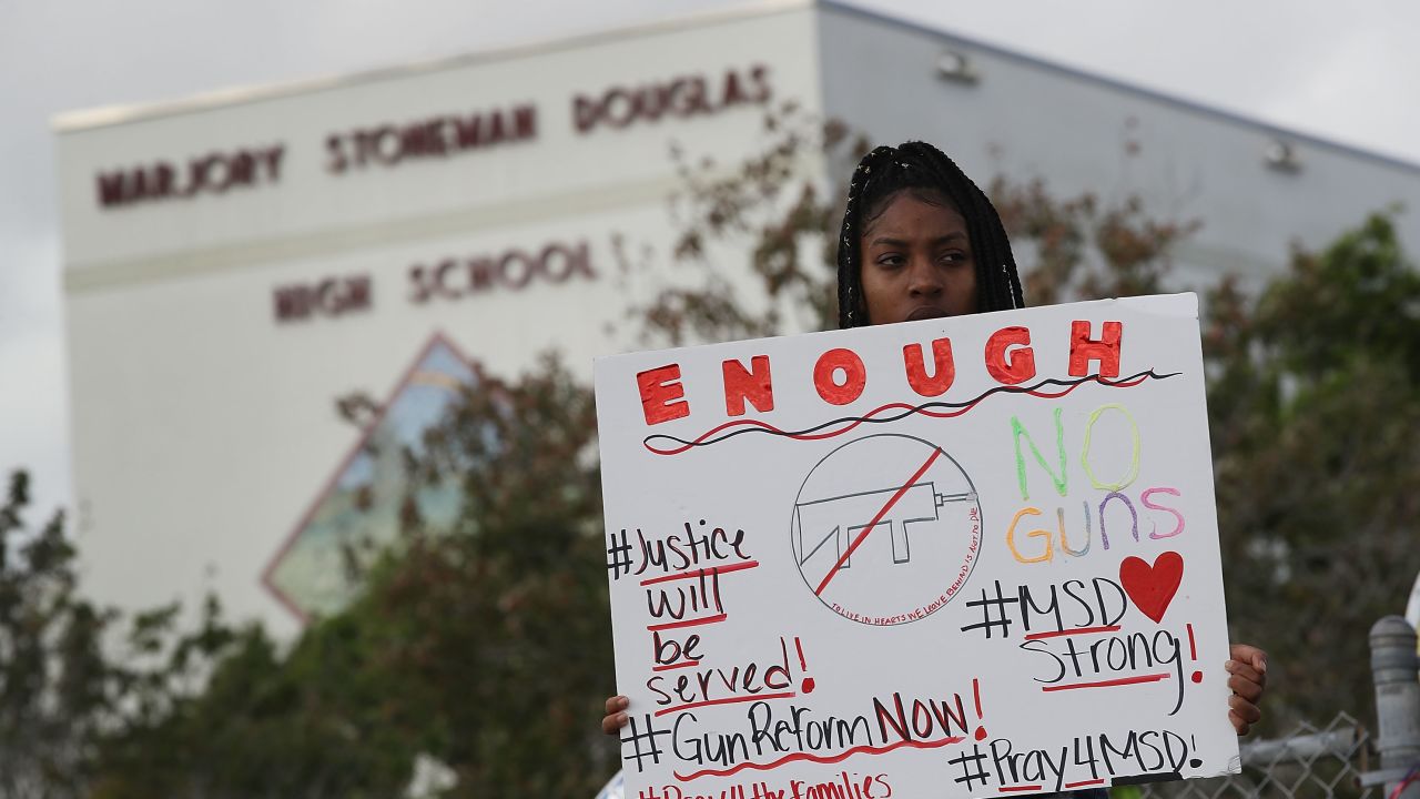 Tyra Heman, a senior at Marjory Stoneman Douglas High School, holds a sign that reads, 'Enough No Guns,' in front of the school where 17 people that were killed 