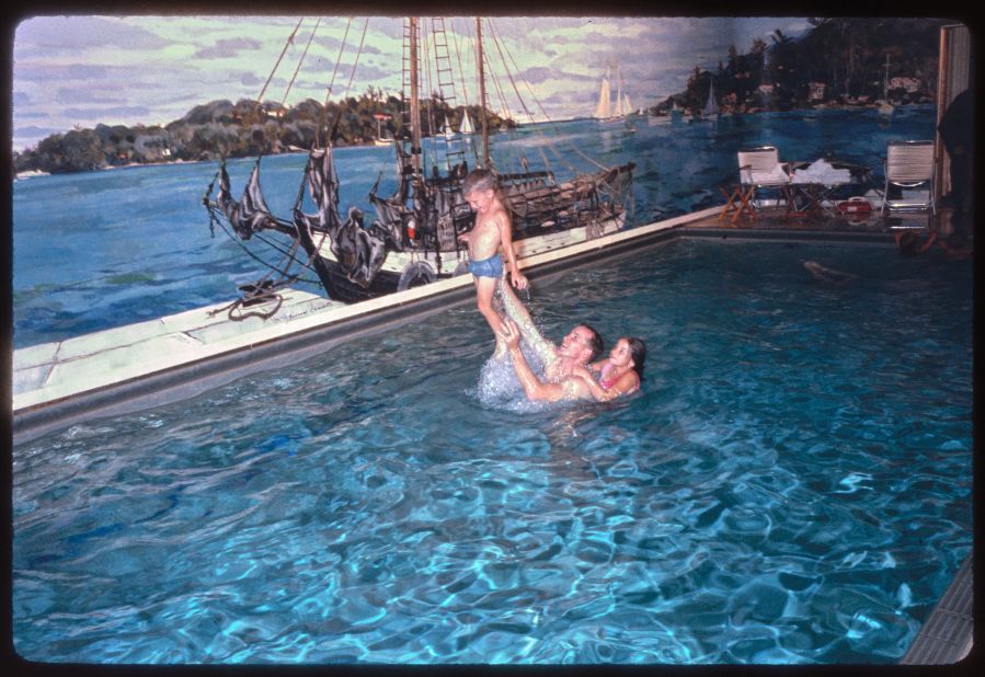 This photograph by Joseph J. Scherschel shows astronauts James McDivitt and Edward White and their families in the White House swimming pool. The McDivitt family is out of frame. They were invited to the White House following the successful Gemini 4 mission to space, which included 62 Earth orbits over four days and the first American spacewalk. The invitation followed their promotion by President Lyndon B. Johnson to the rank of lieutenant colonel the week before at an event at NASA's Manned Spaceflight Center in Houston, Texas, and the visit included an overnight stay at the White House. This pool was installed during the Franklin Roosevelt administration and was covered over during the Richard M. Nixon administration to create the Press Room.