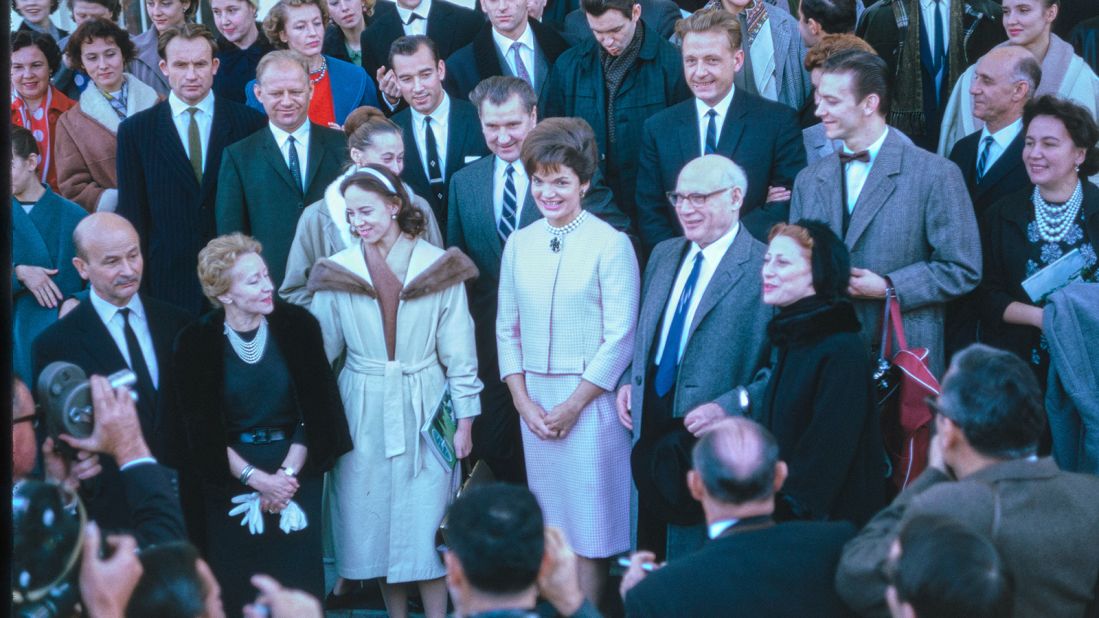 This photograph shows visitors on the North Portico after exiting the White House following a tour. First Lady Jacqueline Kennedy greets the group and poses for pictures.