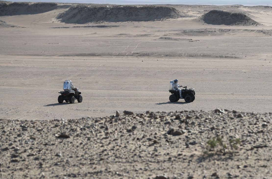 Members of the AMADEE-18 Mars simulation mission ride all-terrain vehicles while wearing spacesuits in Oman's Dhofar desert.