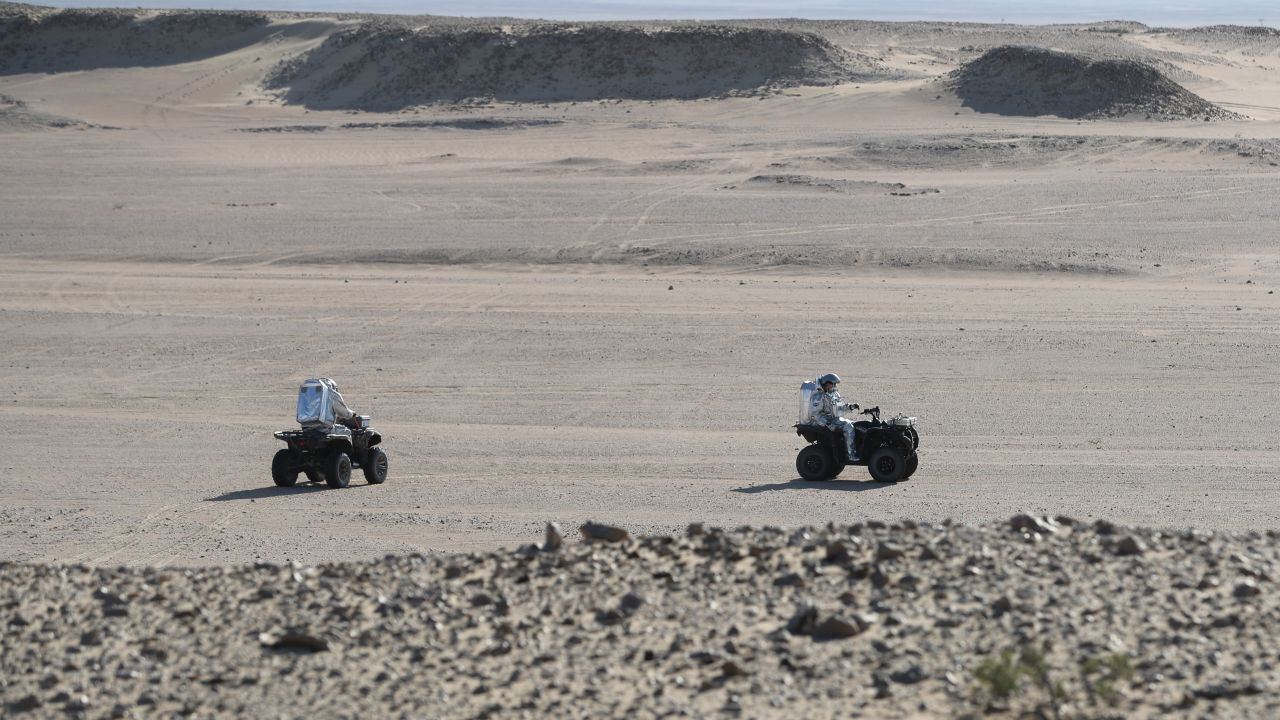 Members of the AMADEE-18 Mars simulation mission ride all-terrain vehicles while wearing spacesuits in Oman's Dhofar desert.