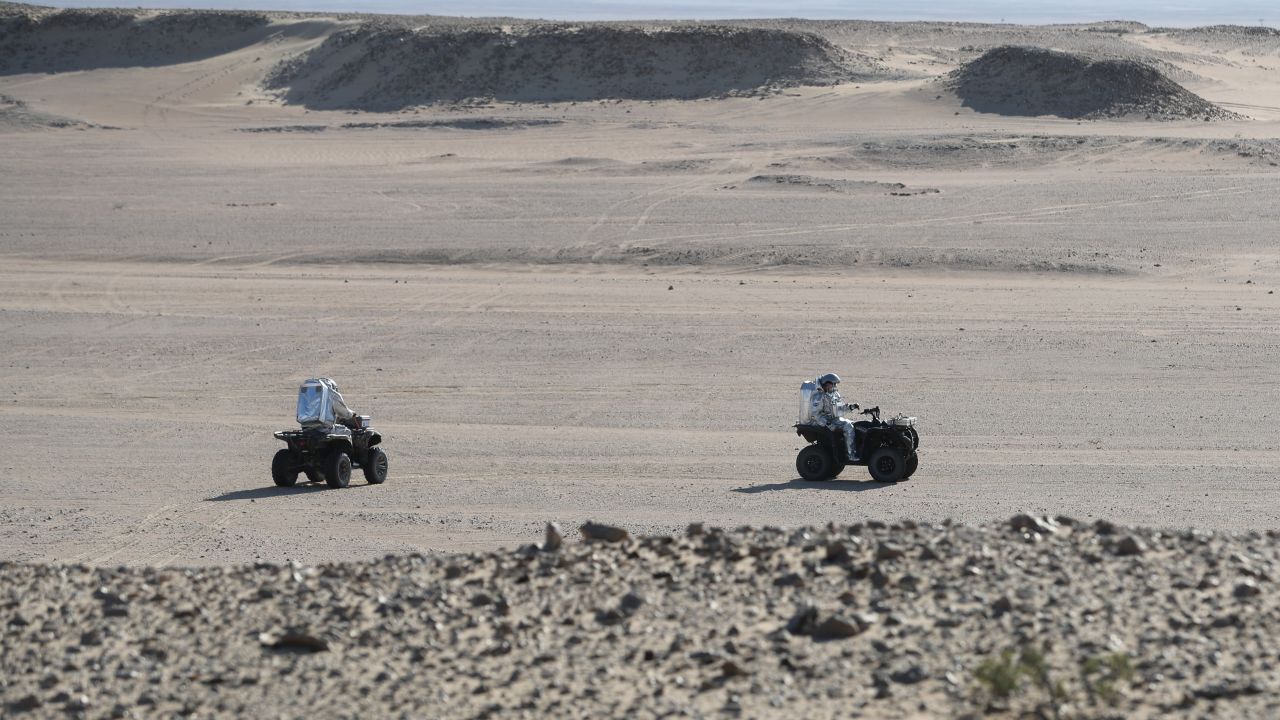 Members of the AMADEE-18 Mars simulation mission ride all-terrain vehicles while wearing spacesuits in Oman's Dhofar desert.