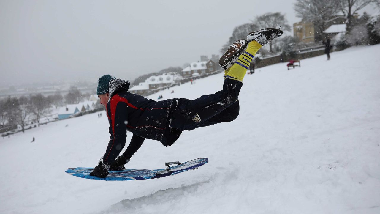 A young man takes a running jump down a snow covered hill with his sled on February 27, 2018 in Rochester, Kent.