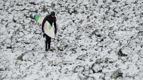 A surfer walks over snow-covered rocks after surfing in Redcar, northeast England. 