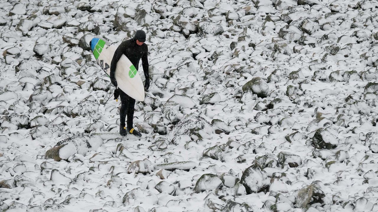 A surfer walks over snow-covered rocks after surfing in Redcar, northeast England.