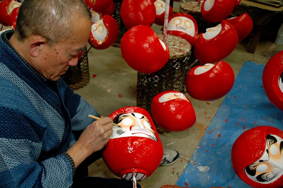 An artisan paints features onto the face of a Daruma doll.