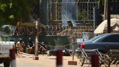 Security personnel take cover as smoke billows Friday from the French Institute in Ouagadougou.