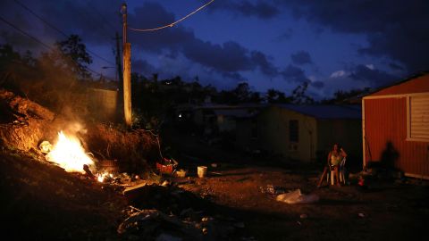 A resident sits outside her home, which lacks electricity, as a trash fire burns in San Isidro, last December.