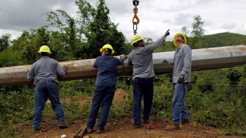 Puerto Rico Electric and Power Authority workers guide an utility pole raised with a crane to repair a downed power transmission line in Ponce, last November.