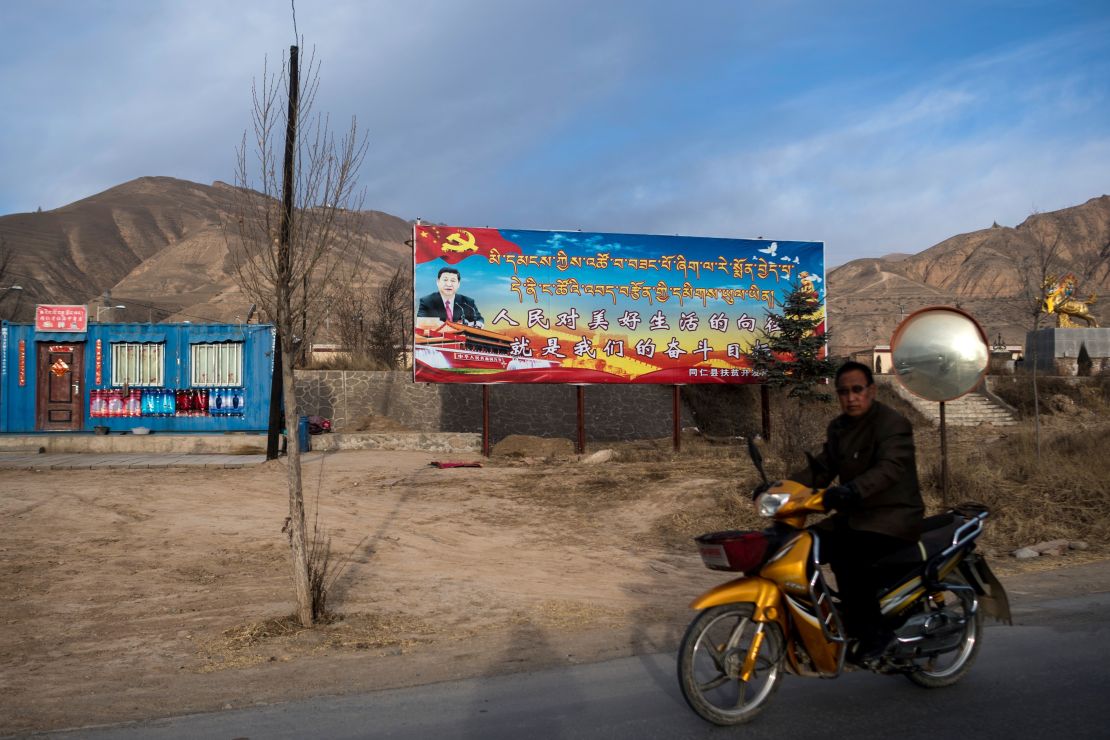 A motorcyclist rides past a propaganda poster showing China's President Xi Jinping next to a freeway outside of Tongren, Qinghai province on March 2, 2018.