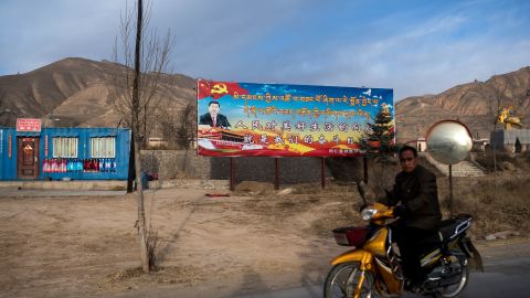 A motorcyclist rides past a propaganda poster showing China's President Xi Jinping next to a freeway outside of Tongren, Qinghai province on March 2, 2018.
