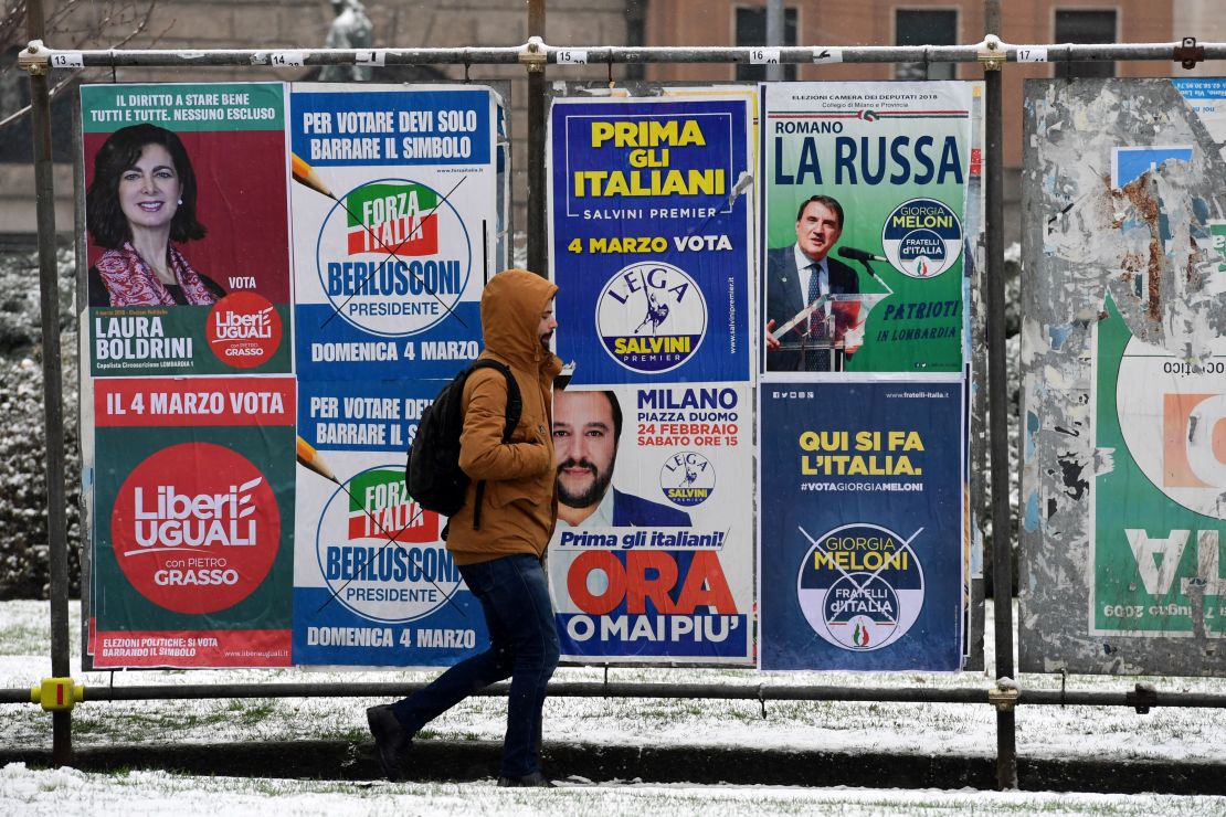 A pedestrian passes in front of election posters in Milan on March 1, 2018.