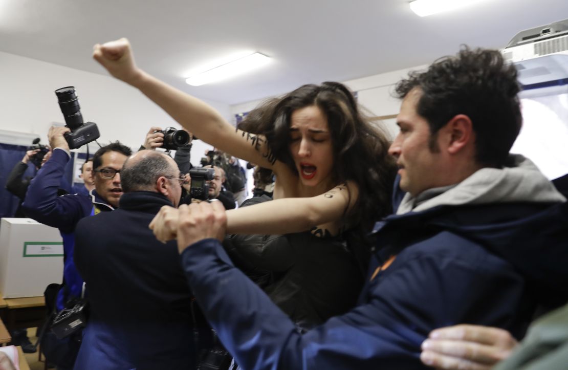 A woman is carried away after staging a protest in the polling station where former Italian premier Silvio Berlusconi was about to vote in Milan, Italy, on Sunday.