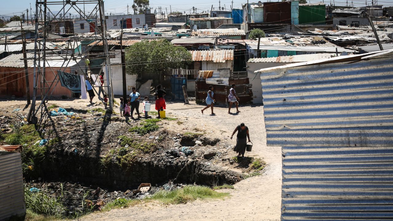 Settlement residents, with buckets in hand, make their way to the shared local tap to collect water. 