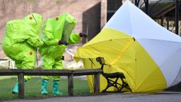 TOPSHOT - Members of the emergency services in green biohazard suits afix the tent over the bench where a man and a woman were found on March 4 in critical condition at The Maltings shopping centre in Salisbury, southern England, on March 8, 2018 after the tent became detached. 
British detectives on March 8 scrambled to find the source of the nerve agent used in the "brazen and reckless" attempted murder of a Russian former double-agent and his daughter. Sergei Skripal, 66, who moved to Britain in a 2010 spy swap, is unconscious in a critical but stable condition in hospital along with his daughter Yulia after they collapsed on a bench outside a shopping centre on Sunday.
 / AFP PHOTO / Ben STANSALL        (Photo credit should read BEN STANSALL/AFP/Getty Images) 