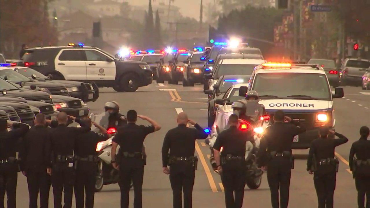 Law enforcement members honor the fallen officer as the coroner's van pulls away. 