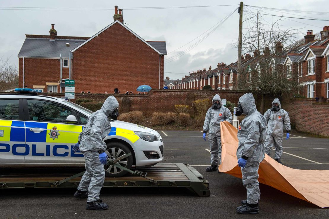 Military personnel wearing protective suits remove a police car and other vehicles from a public car park on March 11, 2018, in Salisbury, England.
