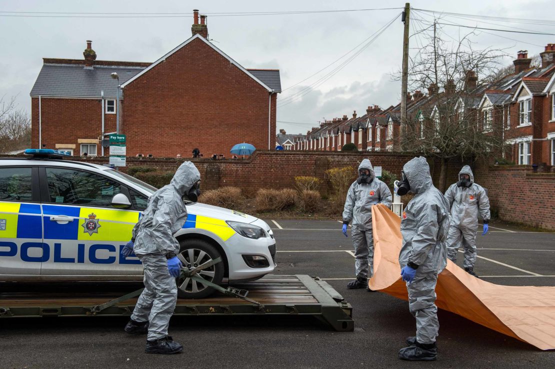 Military personnel wearing protective suits remove a police car from a parking lot as they investigate the poisoning.