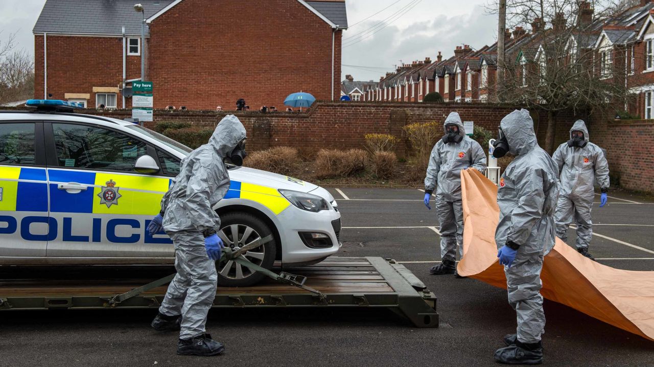 Military personnel wearing protective suits remove a police car and other vehicles from a public car park on March 11, 2018, in Salisbury, England.