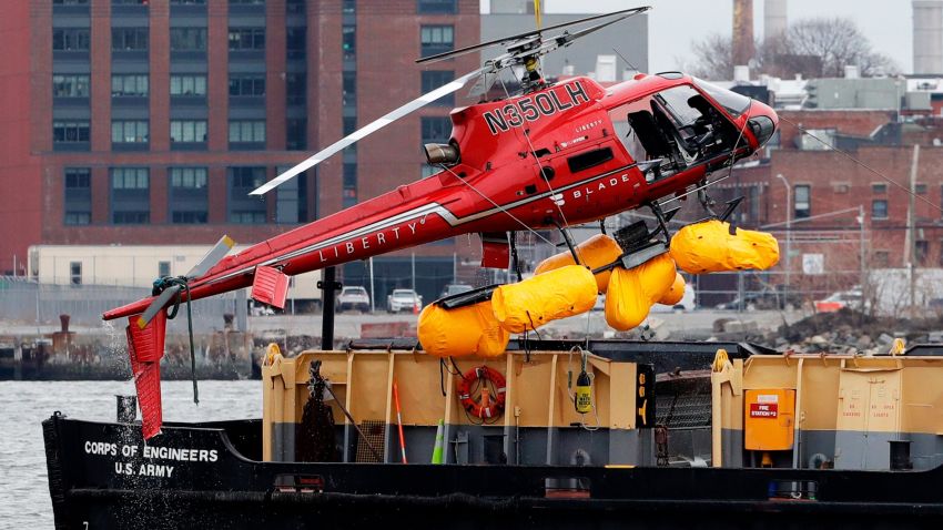 A helicopter is hoisted by crane from the East River onto a barge, Monday, March 12, 2018, in New York. All five passengers aboard a helicopter that crashed into New York City's East River were confirmed dead early Monday morning by a NYPD spokesman. The pilot was able to escape the Sunday night crash after the aircraft flipped upside down in the water, officials said. (AP Photo/Mark Lennihan)